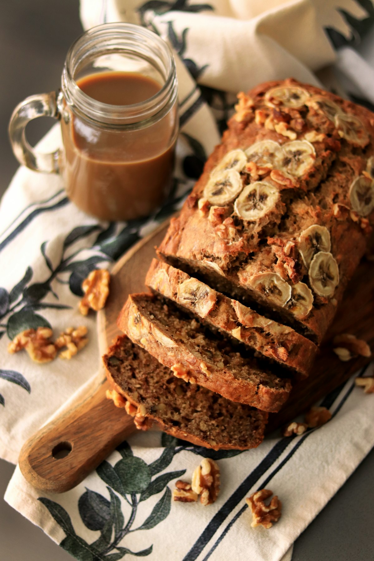 A sliced banana bread loaf topped with banana slices and walnuts