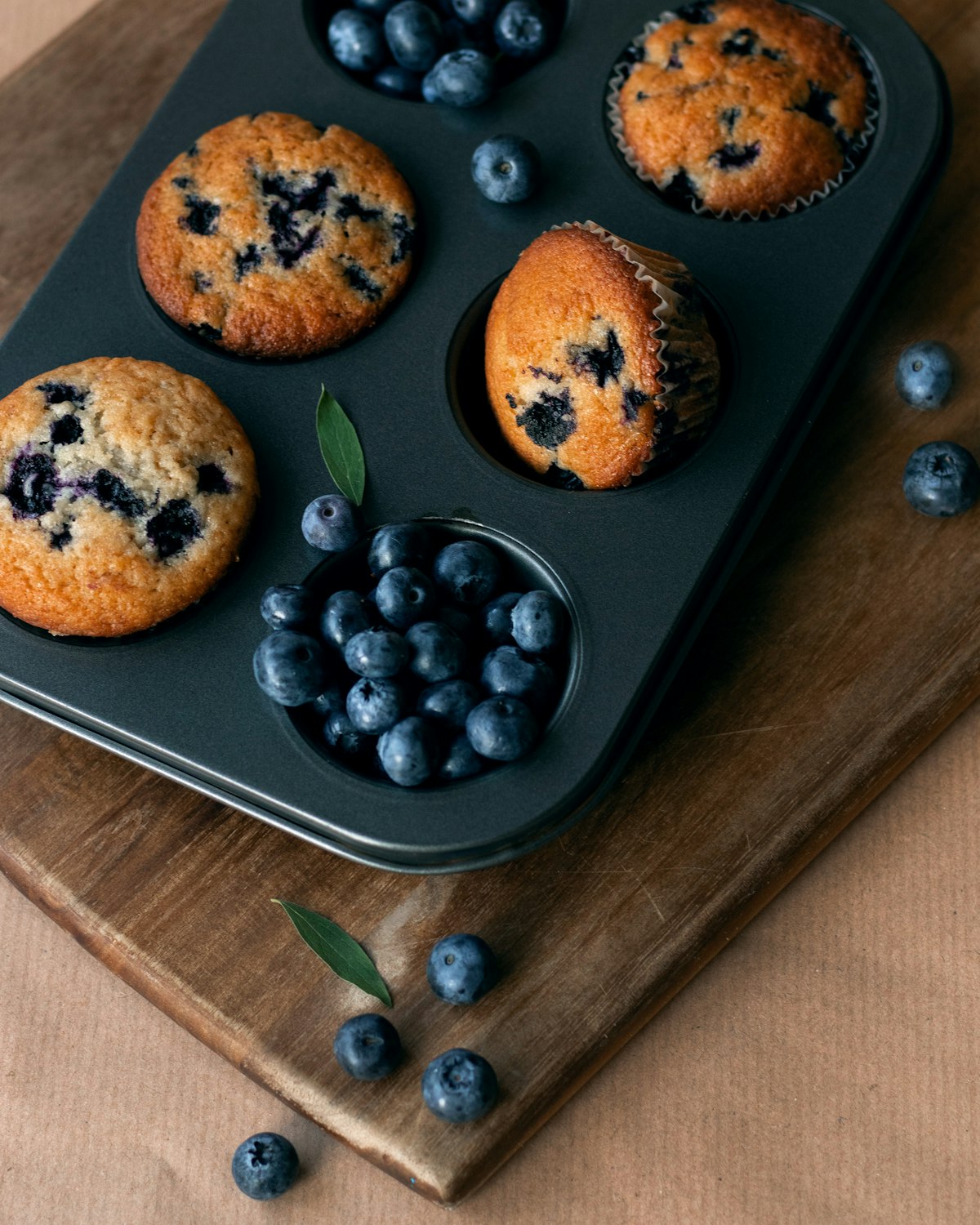Blueberry muffins in a muffin tin surrounded by fresh blueberries