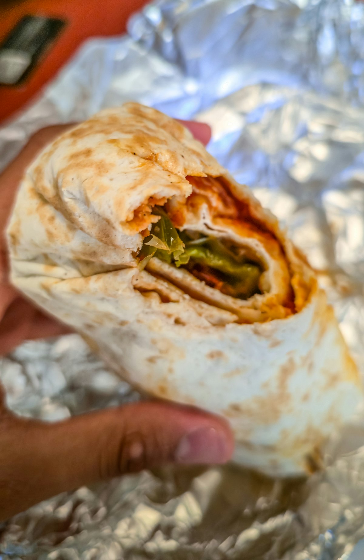 A breakfast burrito wrapped in foil and held in one hand