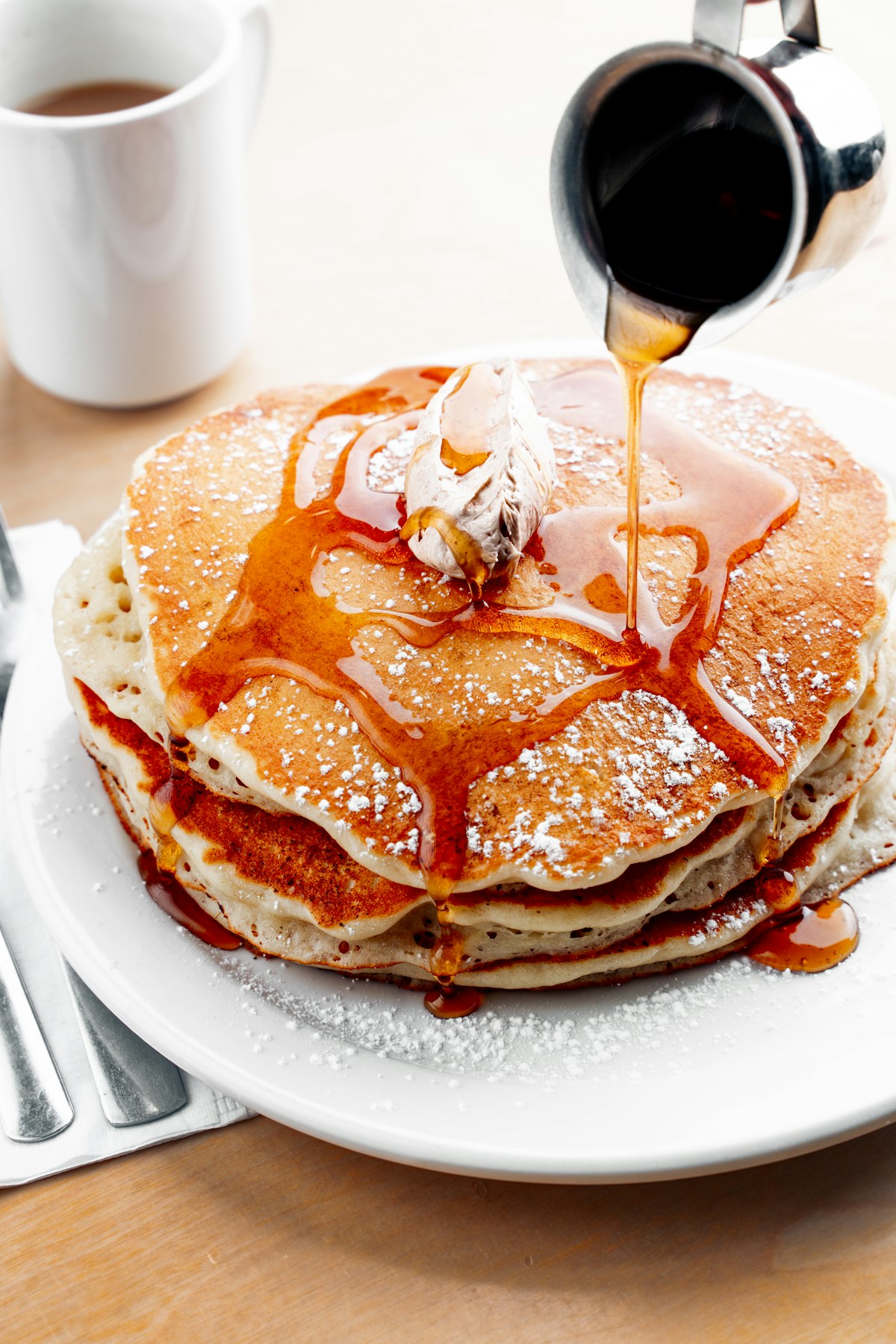 A stack of fluffy buttermilk pancakes with syrup poured over the top