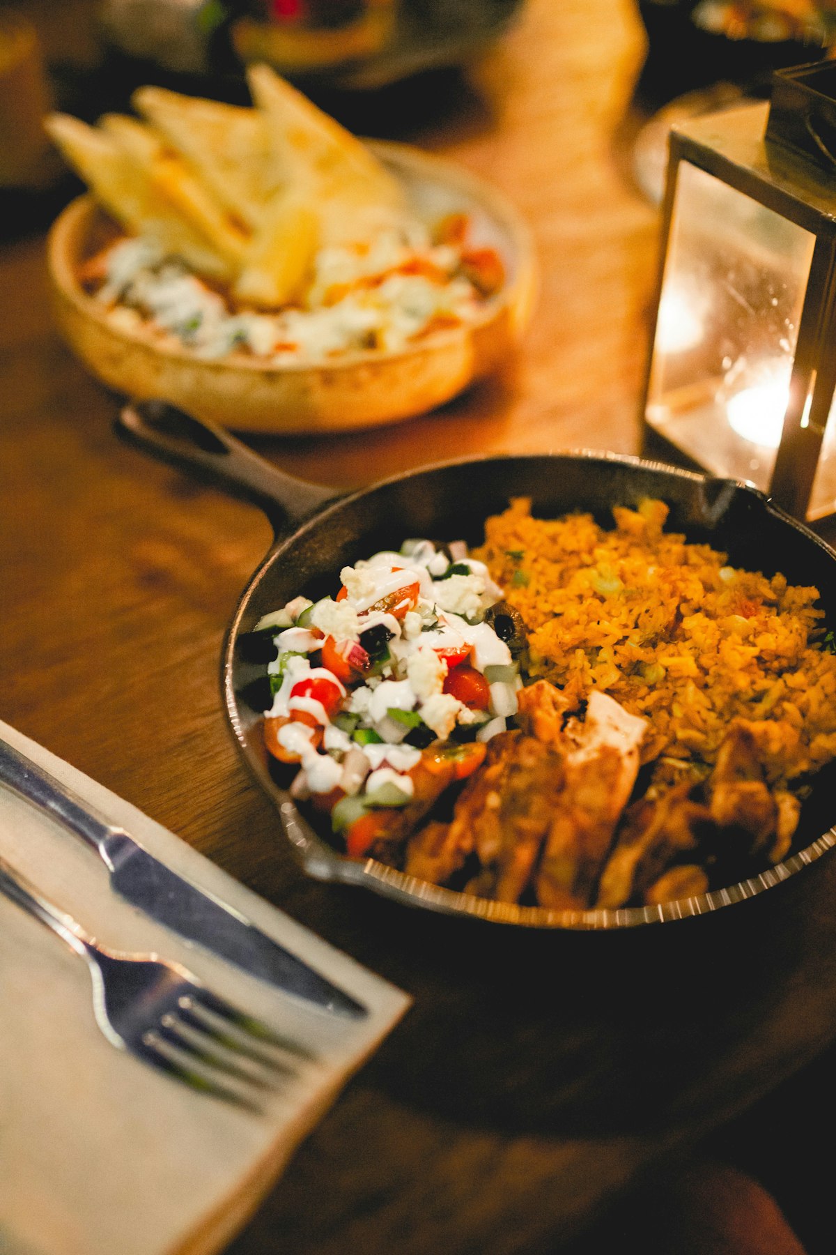 A cast iron skillet of rice and chicken on a warm wooden table