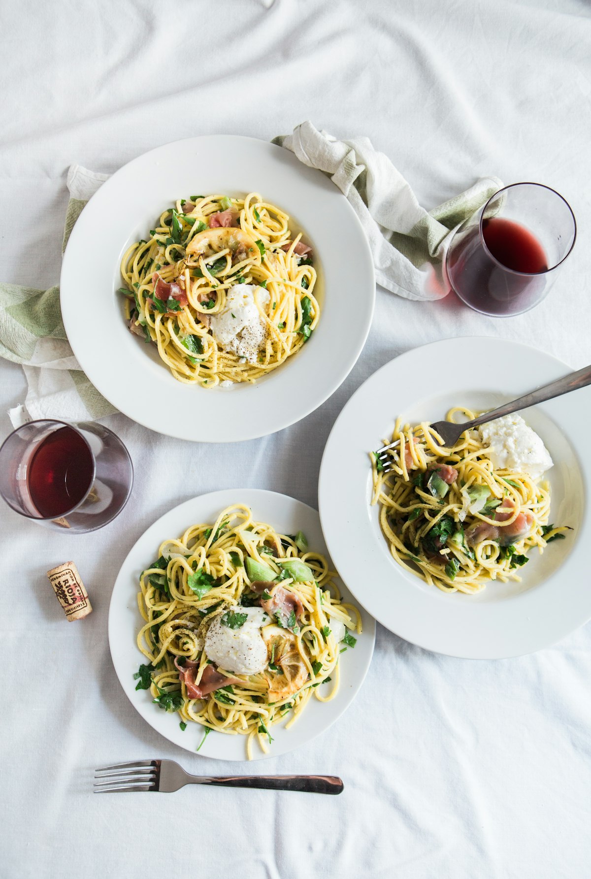 Three plates of spaghetti served with wine on a set table