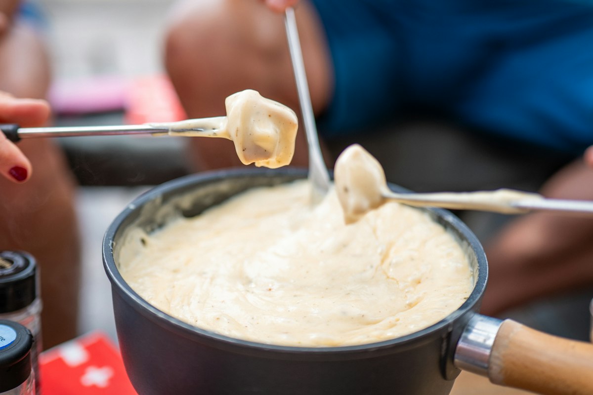 A pot of melted cheese fondue with forks dipping bread into it