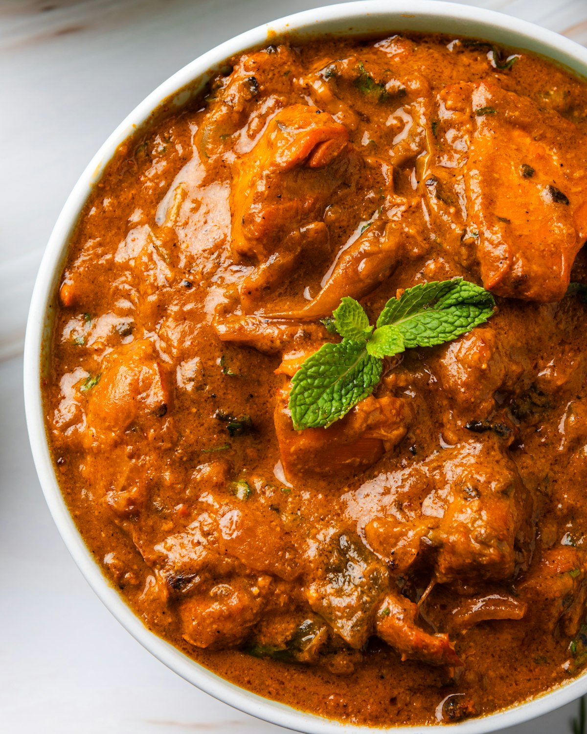 A bowl of creamy orange chicken tikka masala topped with fresh mint