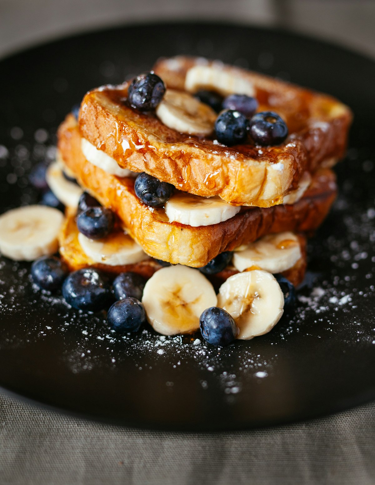 Stacked brioche French toast with blueberries, banana and icing sugar
