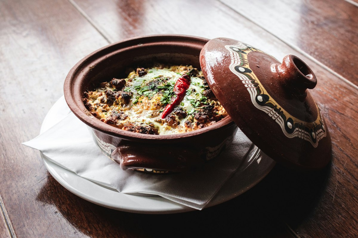 A traditional clay tajine pot with its conical lid set beside the braised stew