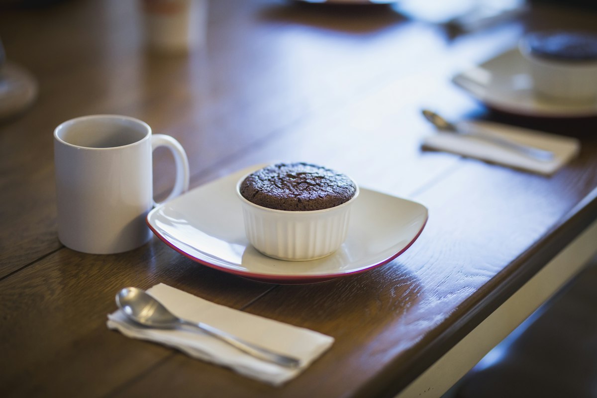 A single chocolate lava cake baked in a ramekin beside a mug
