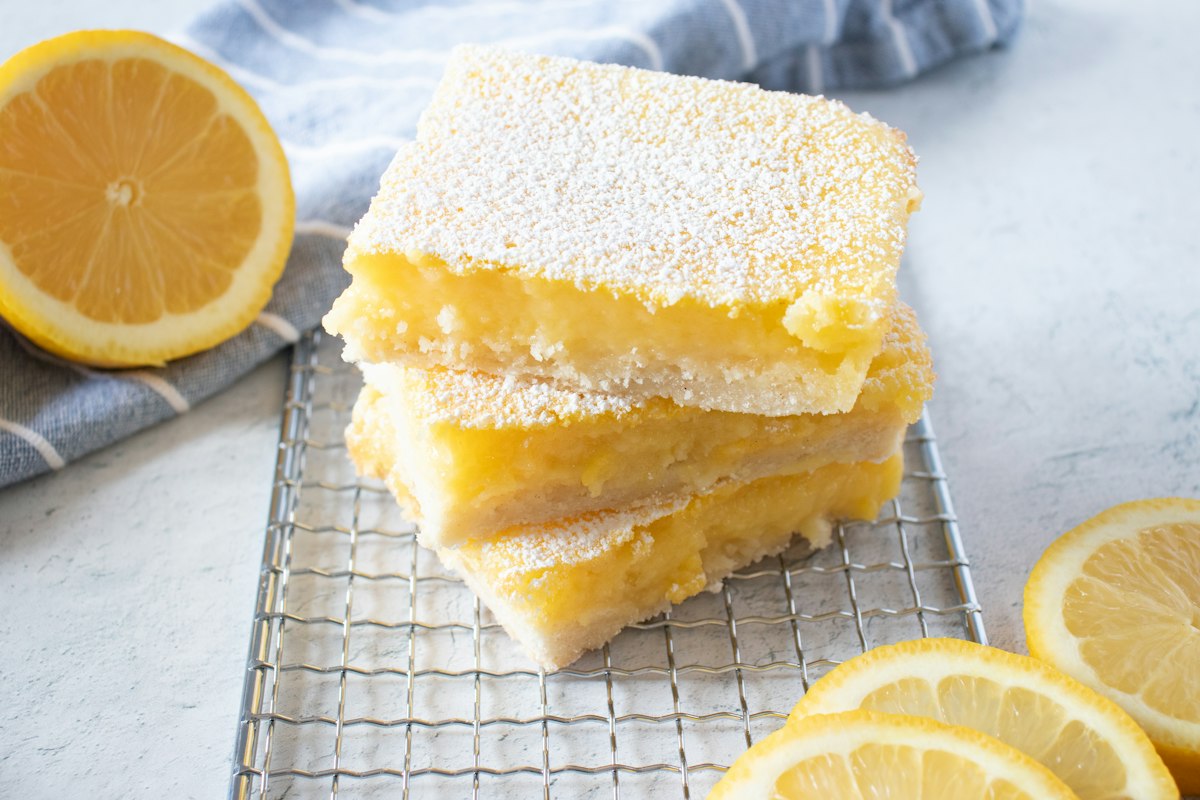 Stacked lemon bars dusted with icing sugar beside fresh lemon slices