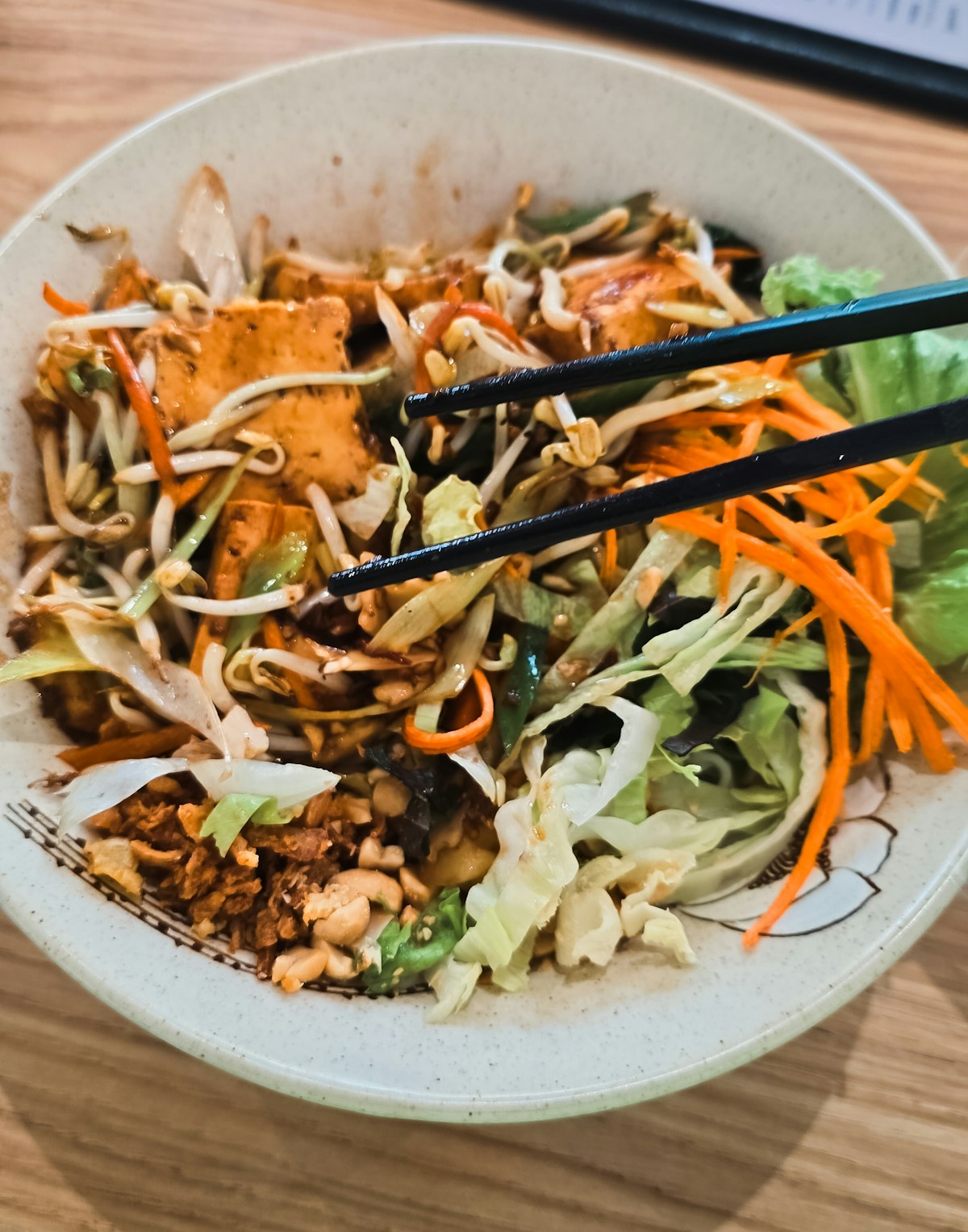 Stir-fried noodles with golden tofu, beansprouts and vegetables, lifted with chopsticks