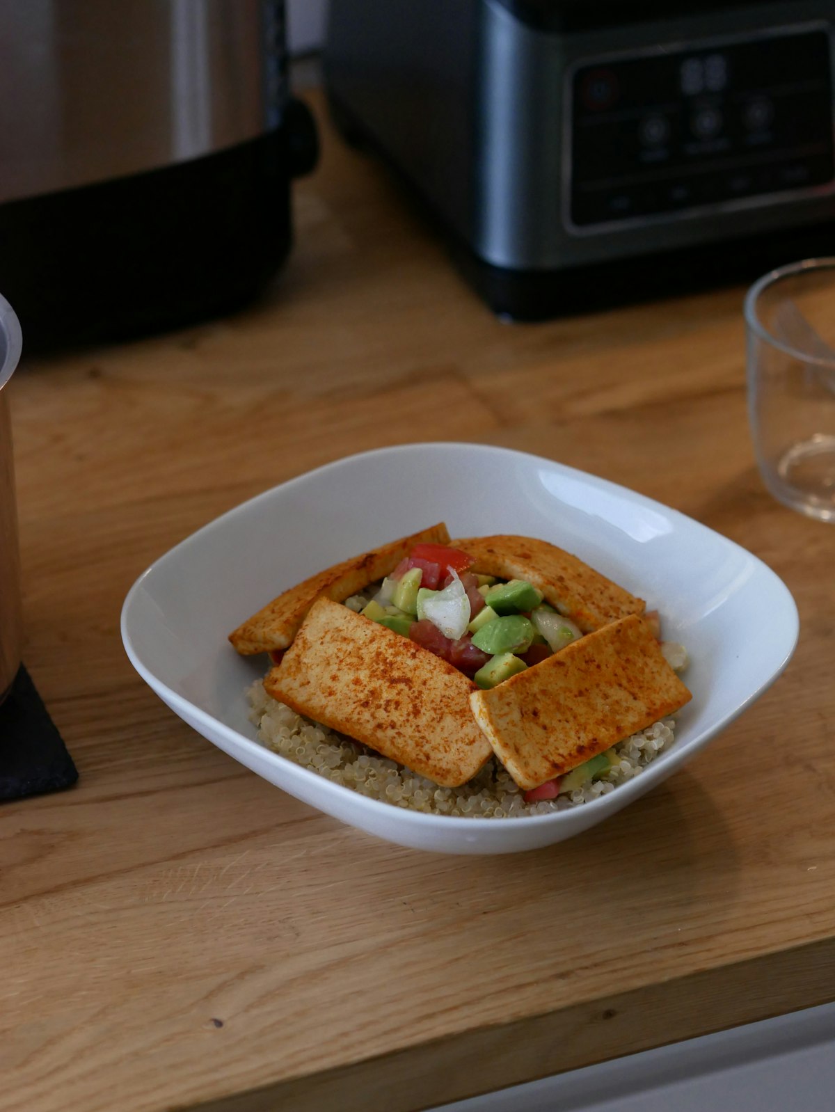 A quinoa bowl topped with golden tofu and avocado salsa