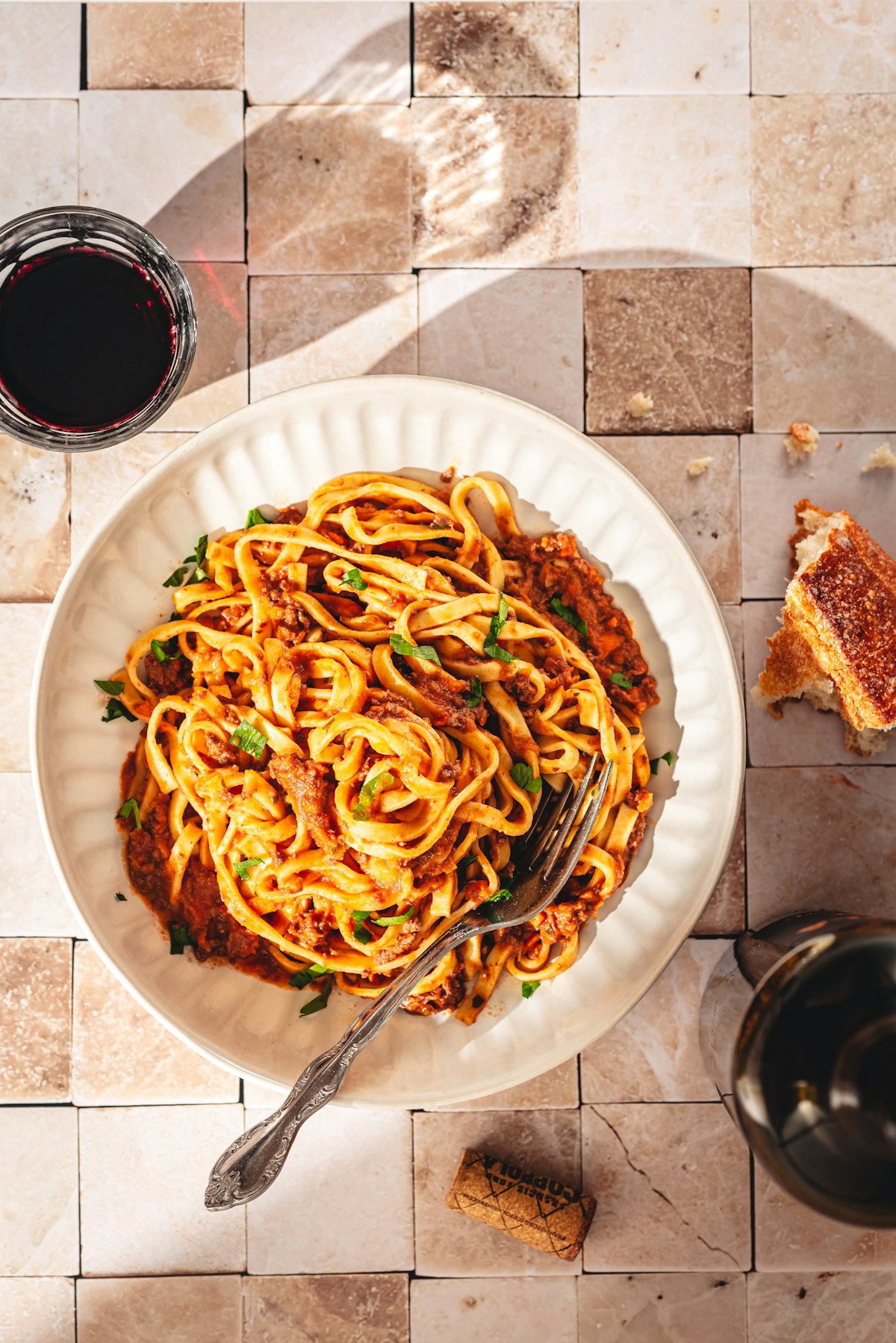 A plate of spaghetti in a rich meat ragu with herbs and a glass of red wine