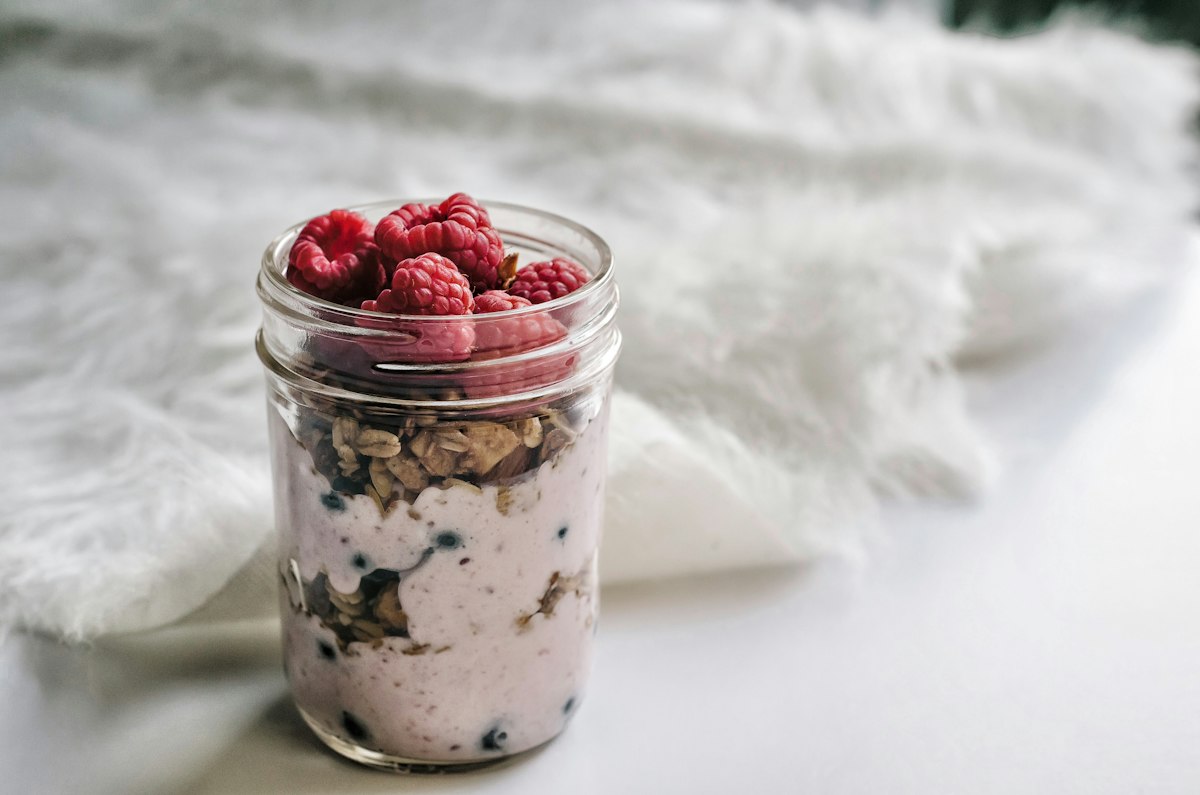 A jar layered with thick yogurt, granola and fresh raspberries